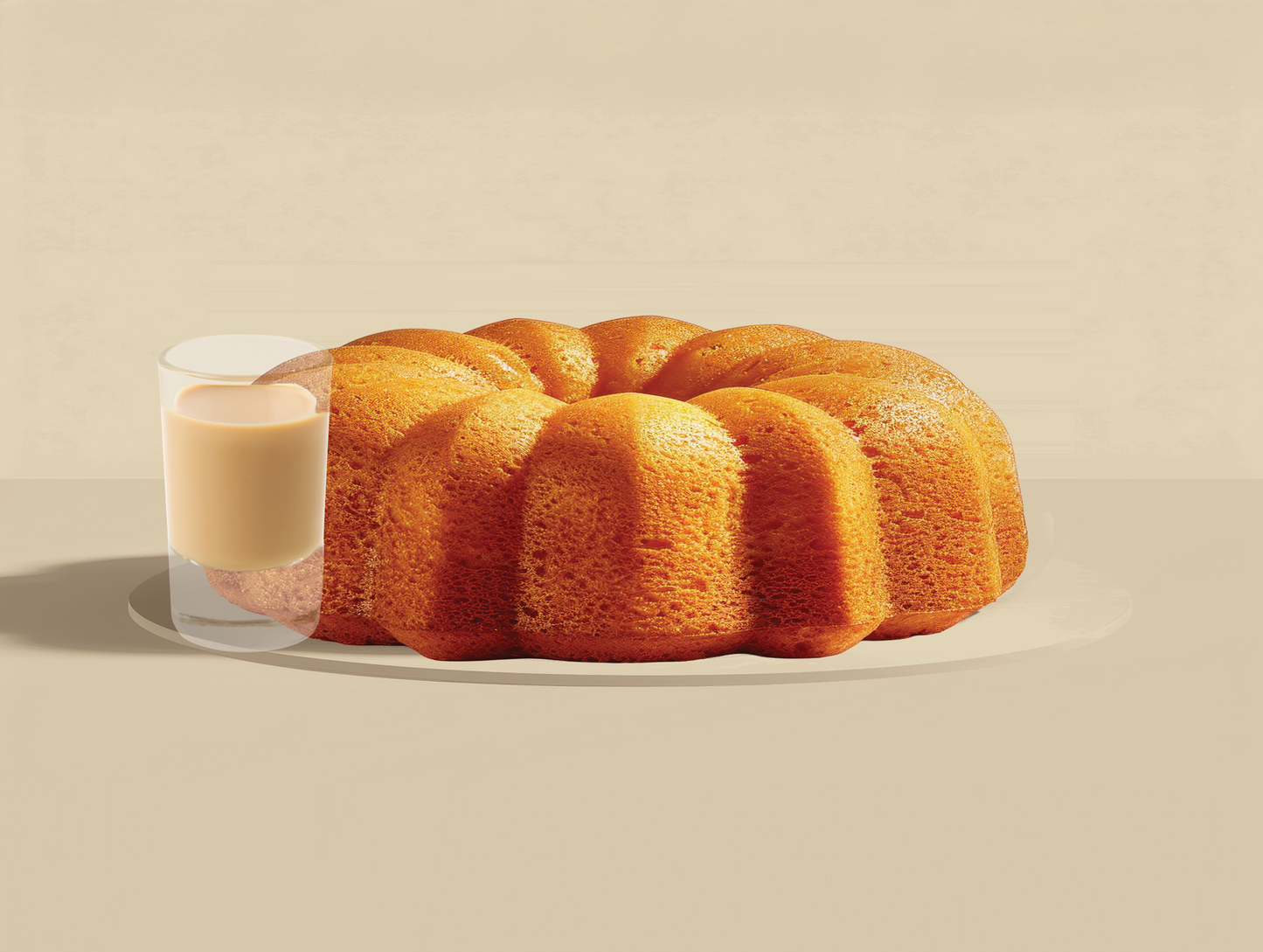 Bundt cake on a plate with a glass of irish cream liqour on a beige background